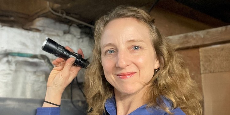 Susannah Krysko holding a flashlight and smiling, wearing a stop pests shirt