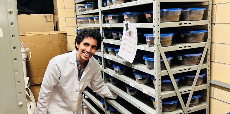 A man reaches onto a shelf. He is wearing a lab coat.