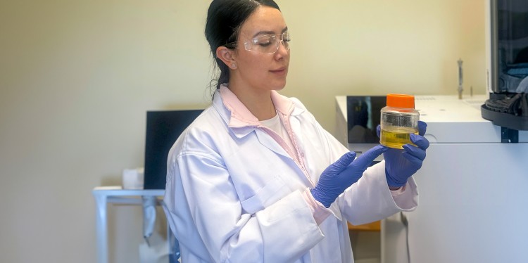 a woman in a lab coat looks at a beaker of liquid