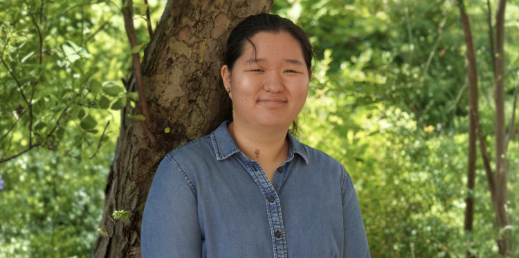 A woman stands in front of a tree smiling.