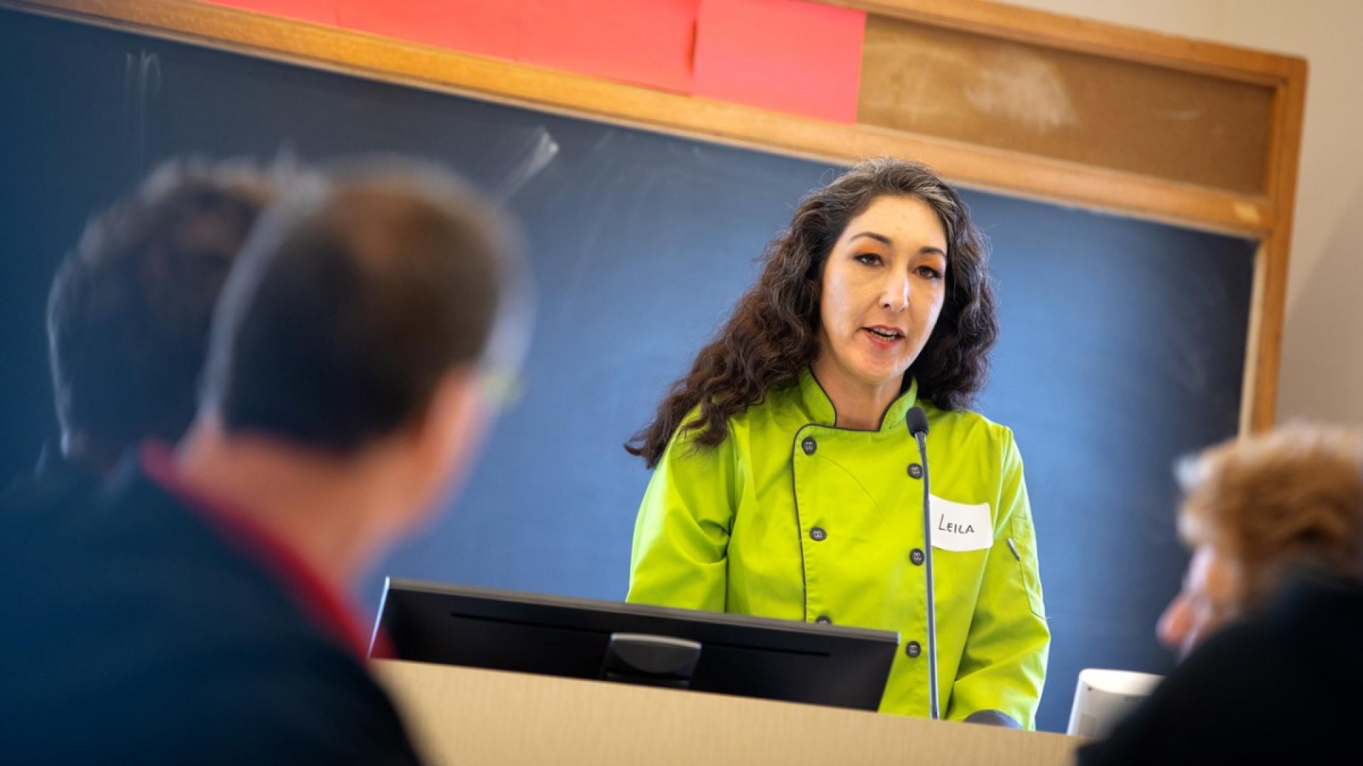 A woman standing at a podium in a green shirt talking to an audience