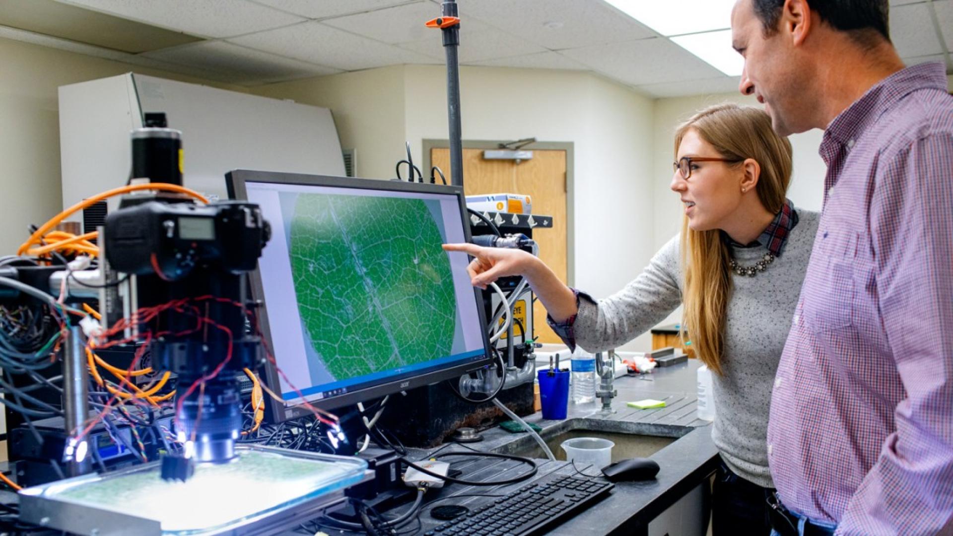 A man and woman stand at a computer gesturing toward it
