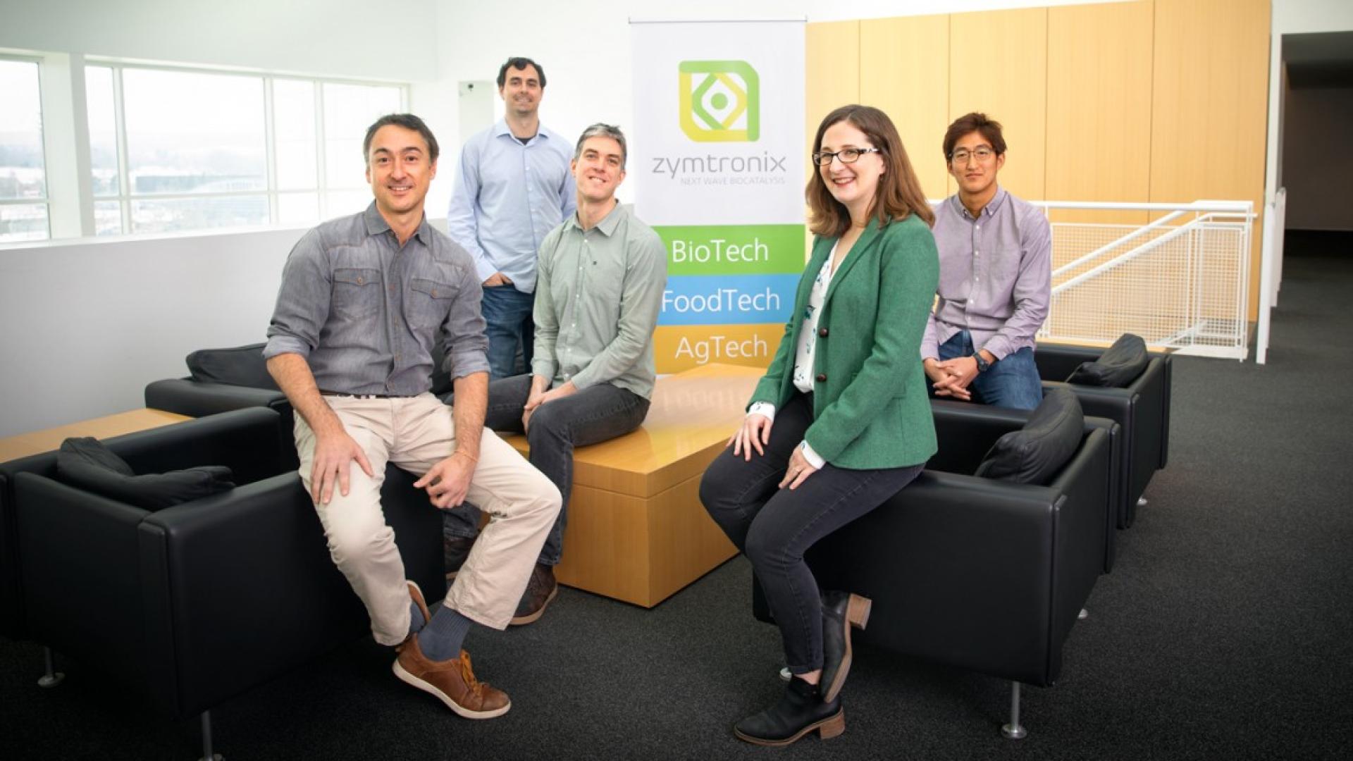 one female and four males standing in an open seating area in a building 