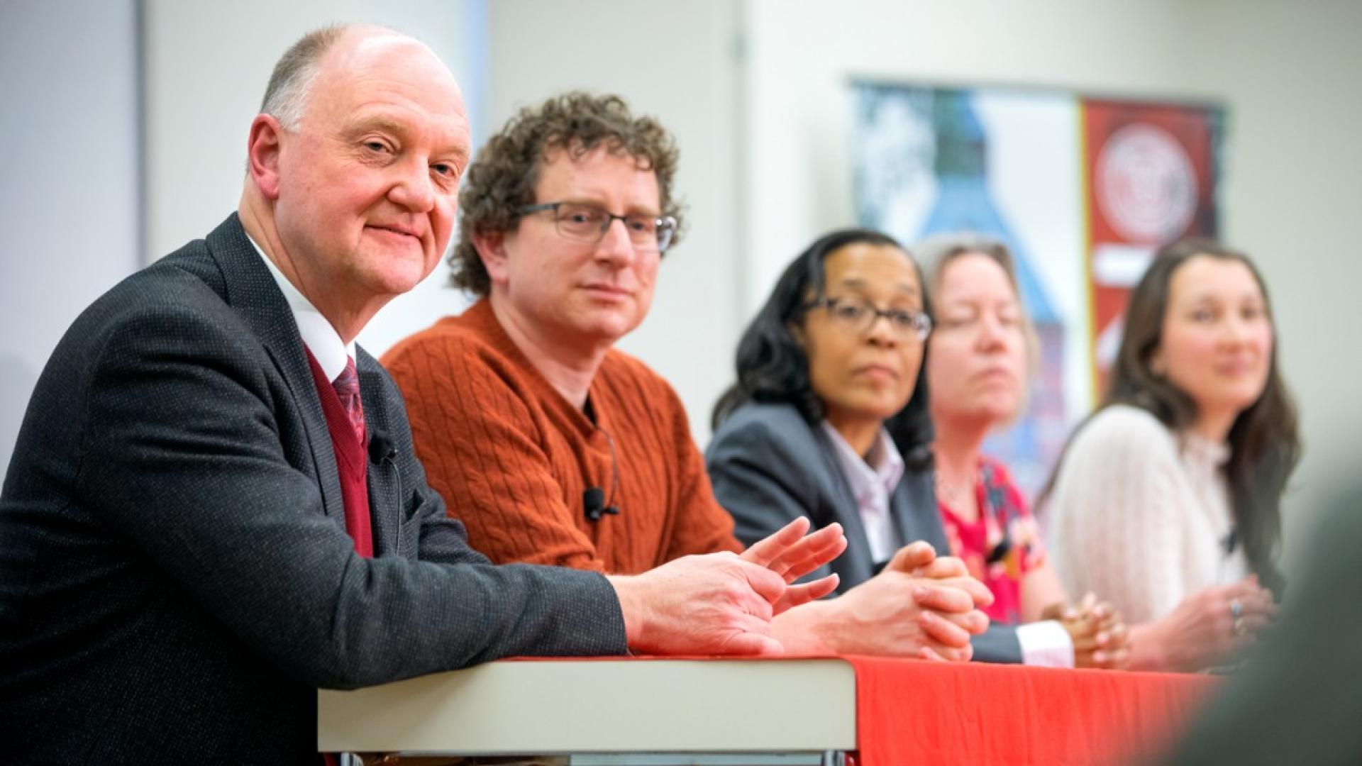 Two men and three women sitting at a table in front of microphones
