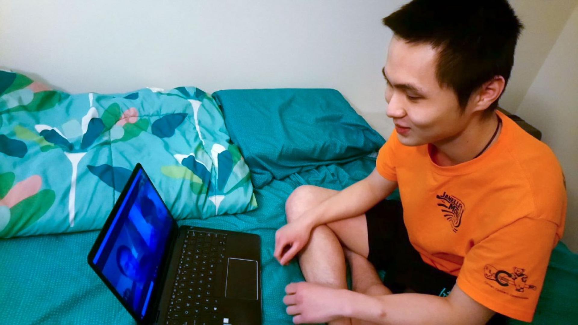 A student sitting on a bed looking at a laptop