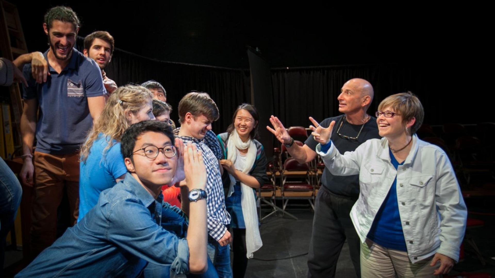 A group of people all act colorfully as two people gesture towards them