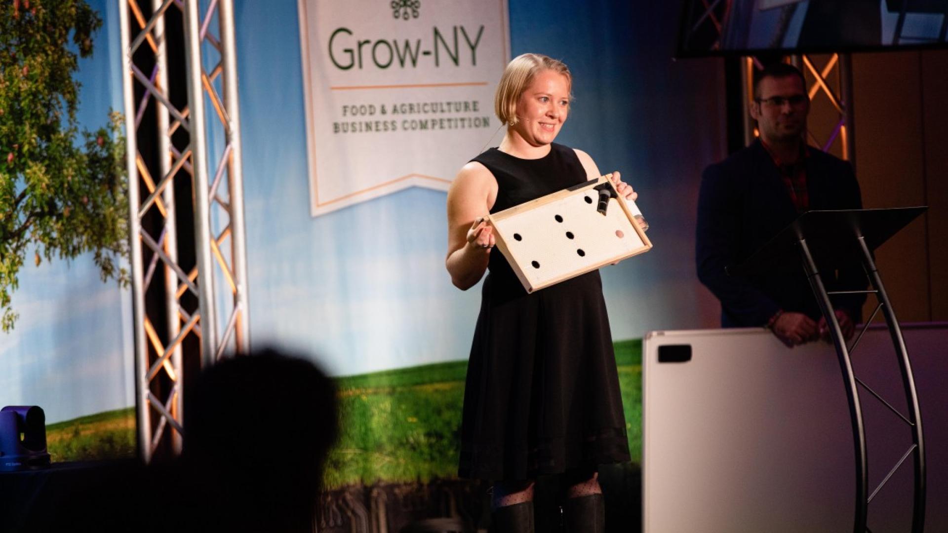 Woman smiles on stage as she presents a project