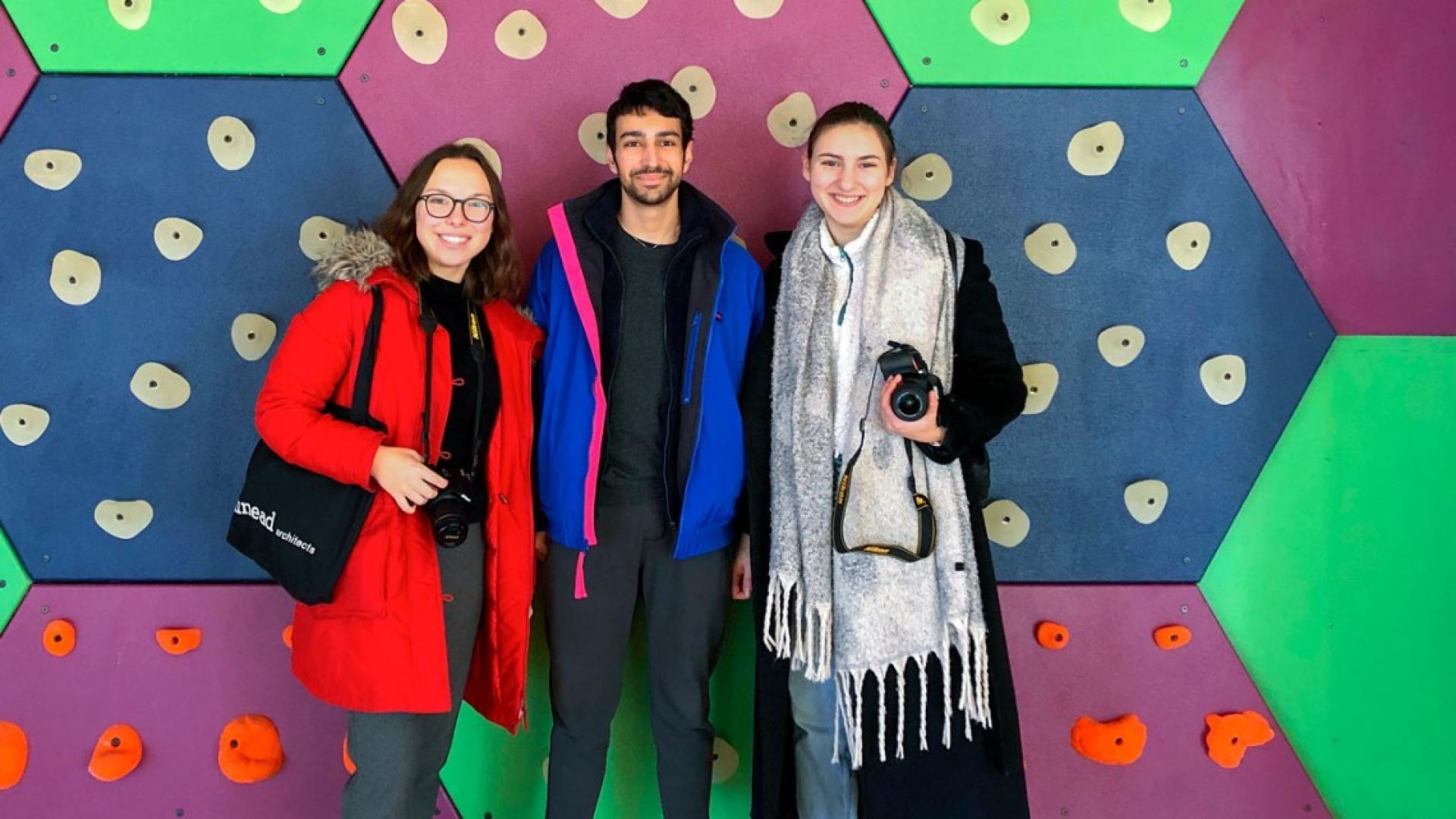 A man and two females standing together with a colorful wall behind them