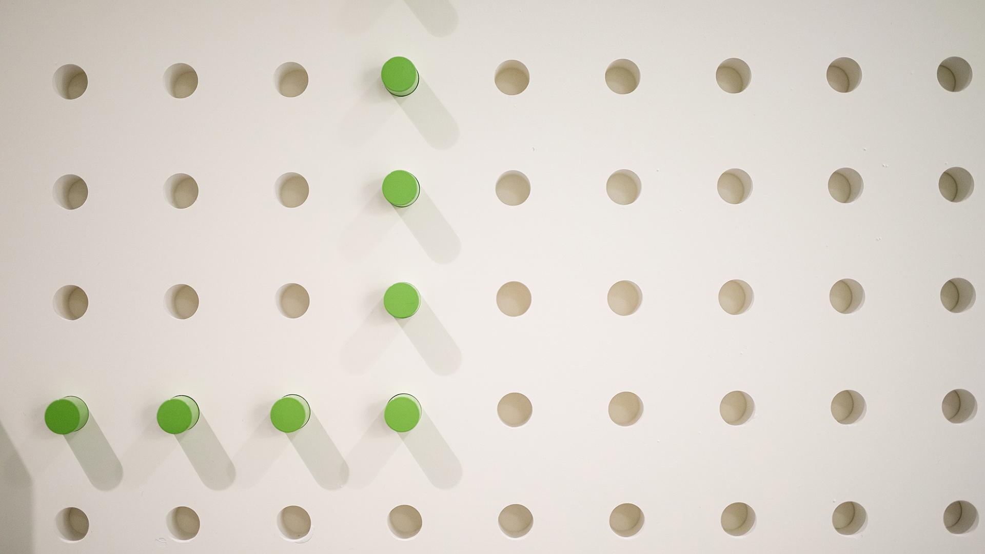 A white wall with green pegs in it