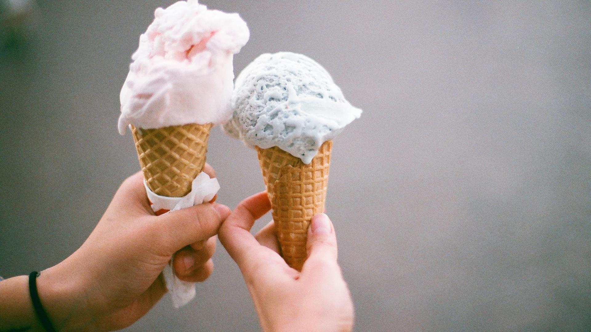Two hands holding ice cream cones. 