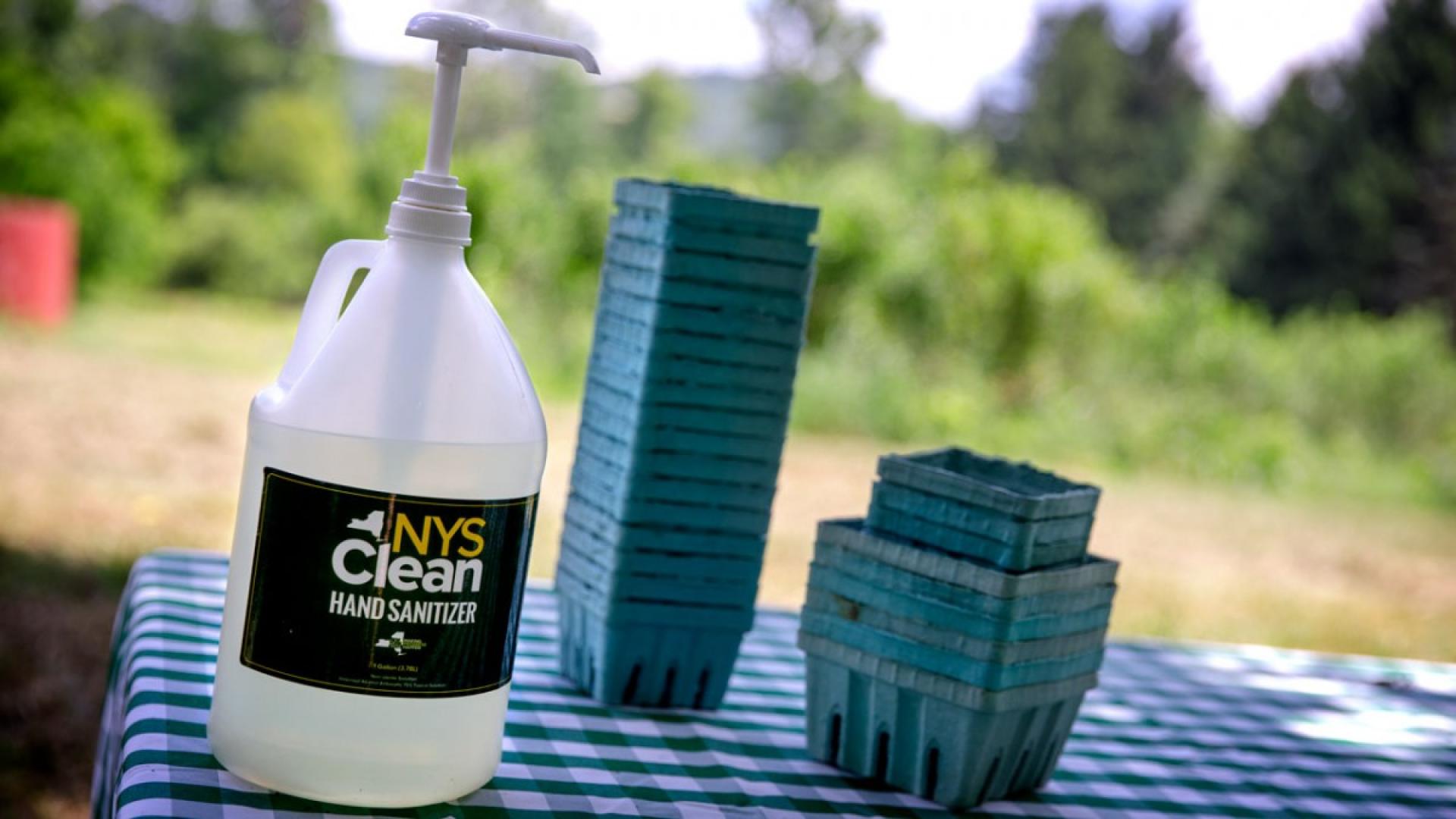 A large pump bottle of hand sanitizer on a table next to green cardboard blueberry boxes 