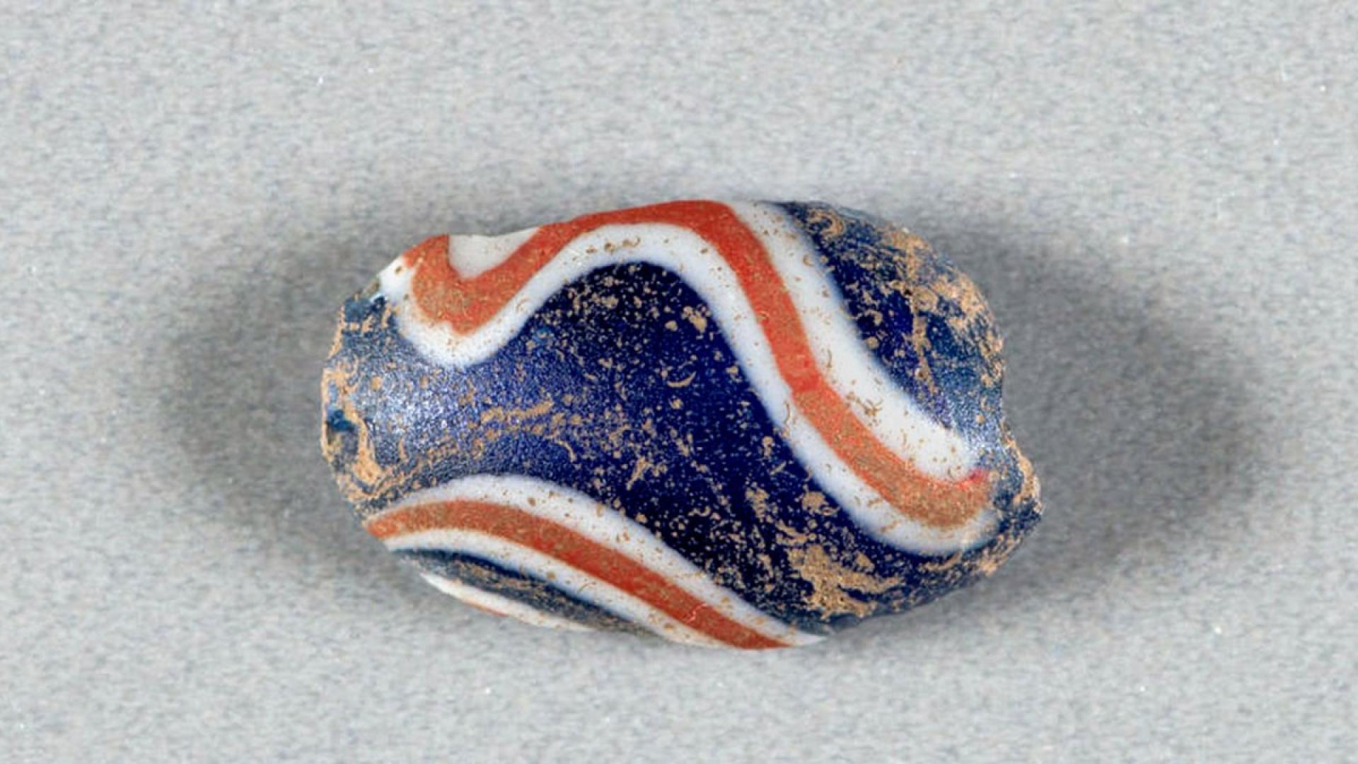 A blue bead with white and orange curving lines