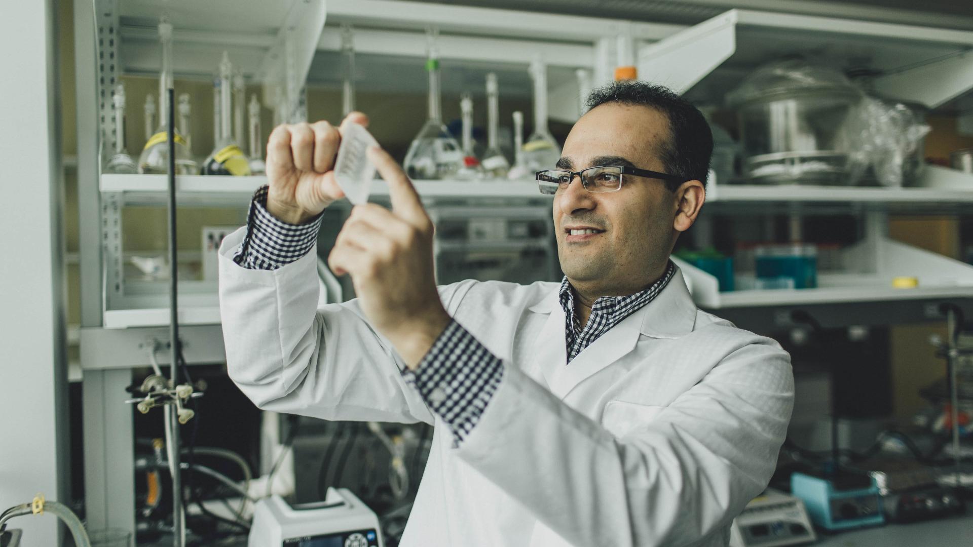 A man in a lab coat holds a slide up to the light.