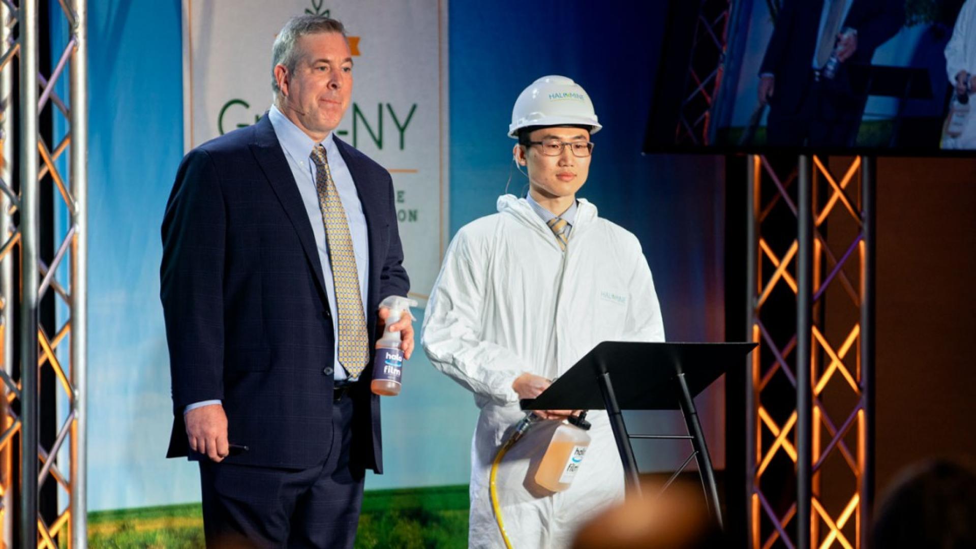 Two men stand on stage at a conference 
