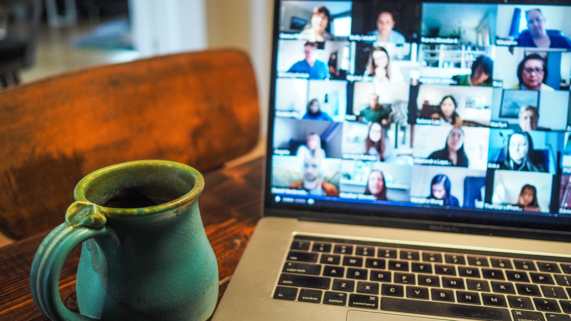 A zoom call pulled up on a laptop with a green mug next to it on the table