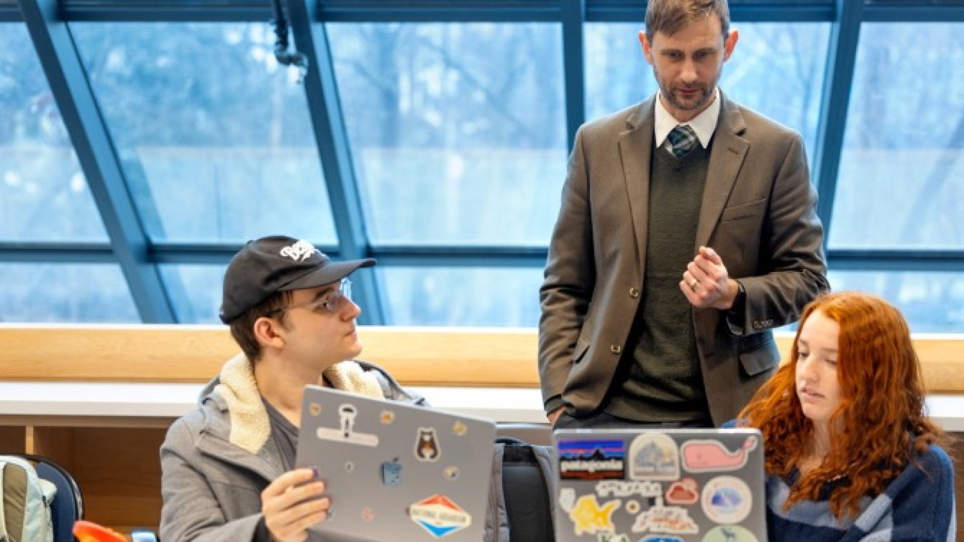 Ault stands behind two students who are showing him something on their laptops.