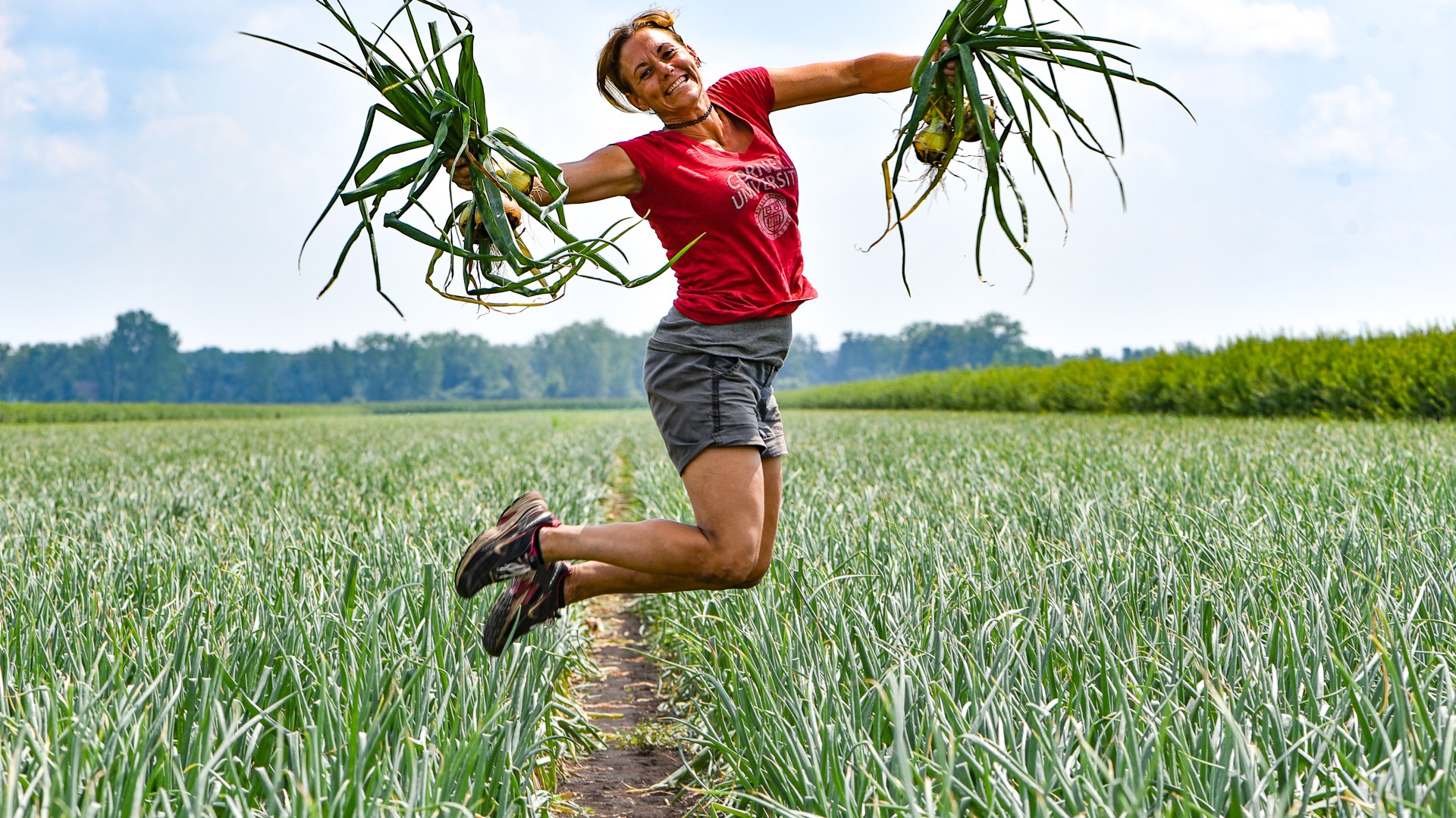 Christy Hoepting jumping in a field of onions, with onions in her hands
