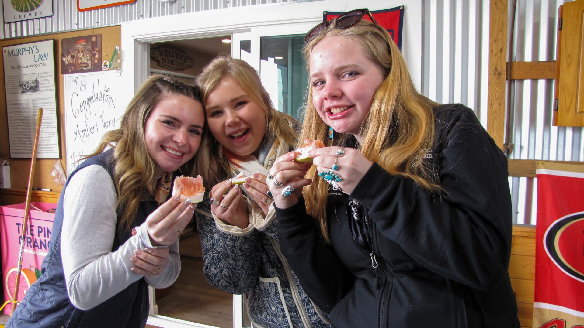 three woman stand together eating orange slices
