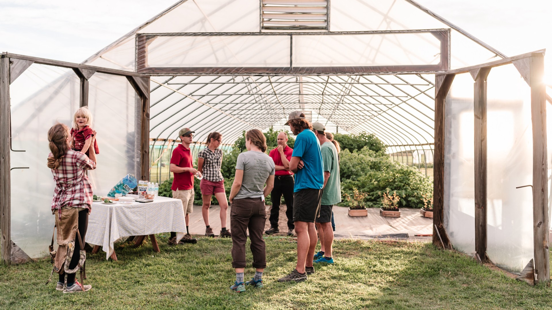 a group of people in front of a high tunnel with crops