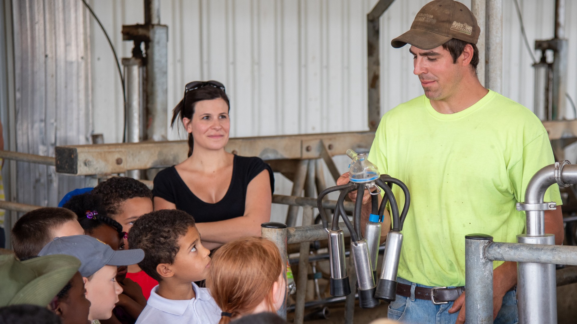 Cheryl on a farm tour with schoolkids. A farmer holds a miling machine in his hand, showing it to the kids.
