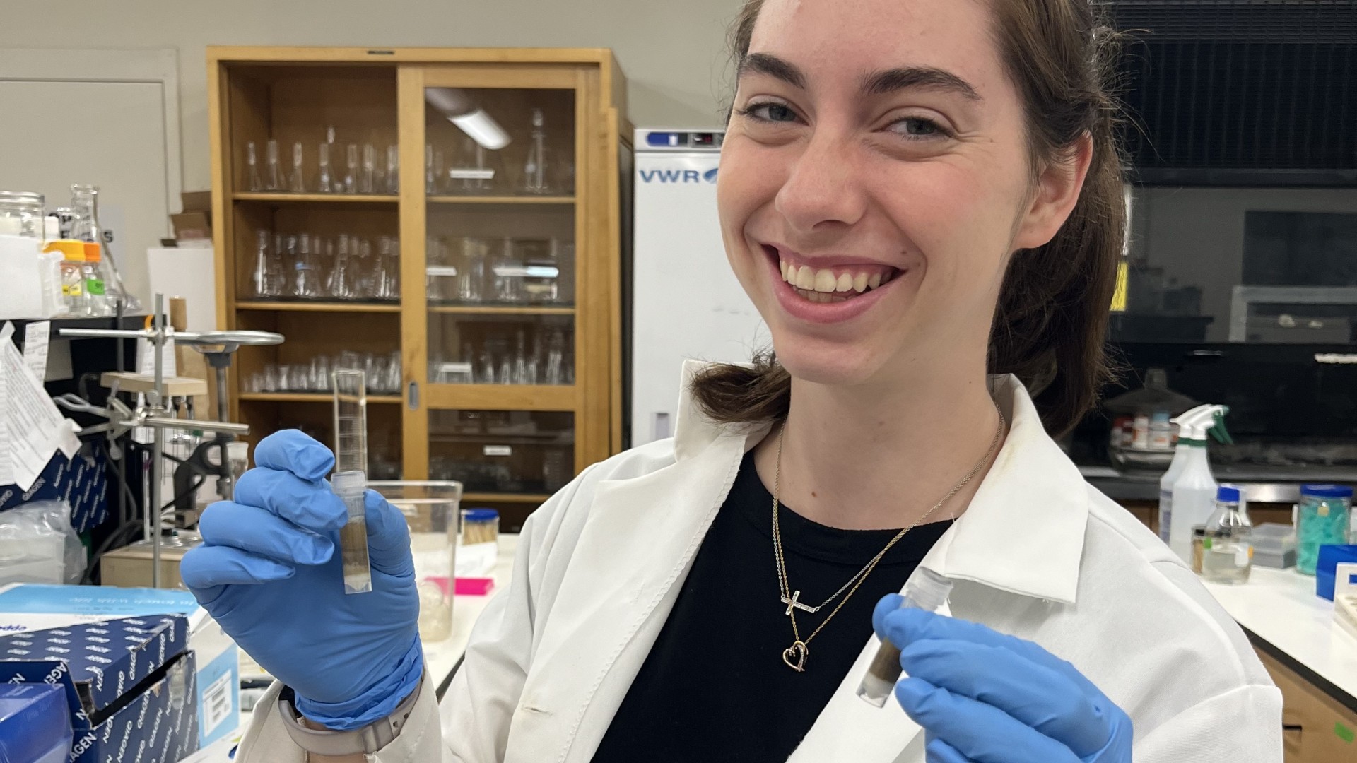 A woman holds two test tubes and smiles.
