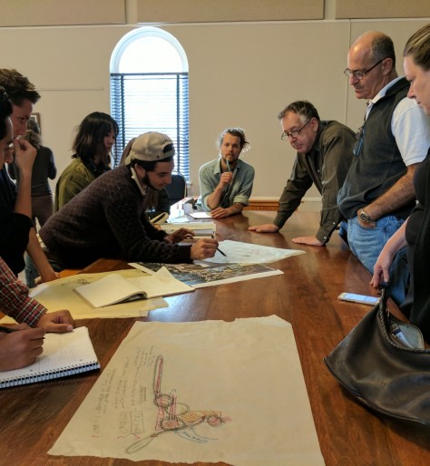 A group of people examine documents over a table.