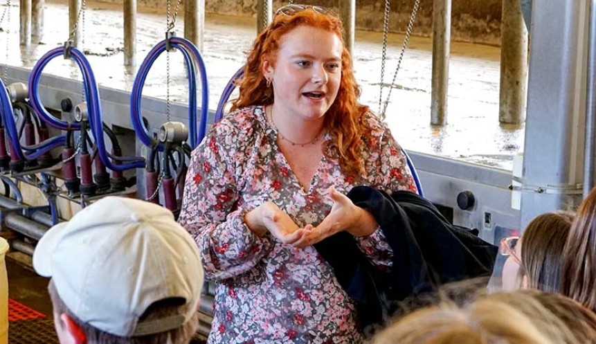 person with red hair speaking to a crowd in a barn