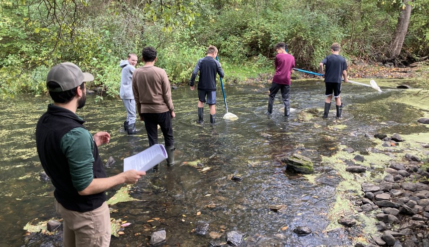 Photograph of six people holding nets walking through a stream.