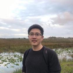 Postdoc Honggang Zhao stands in front of a creek and marsh area.