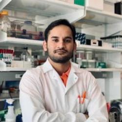 A man in a labcoat stands in front of lab shelves full of bottles
