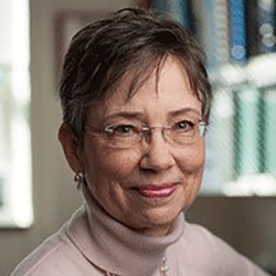 a woman with glasses in a turtleneck in front of a shelf of books
