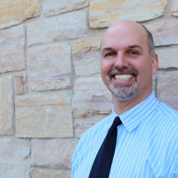Ryan Staychock smiling in front of stone wall blue shirt