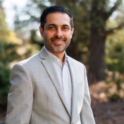 man in light suit stands in front of trees