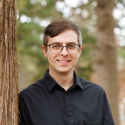 person leaning up against a tree in a black button down shirt