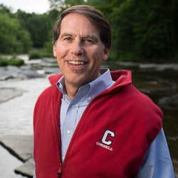 Man in blue shirt and red vest with a creek in the background.