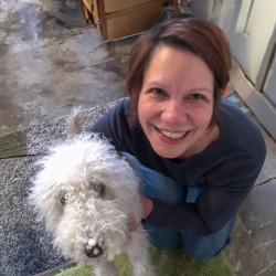 a woman crouches next to a dog and looks up at the camera