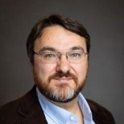 A headshot of a man wearing glasses and a collared shirt