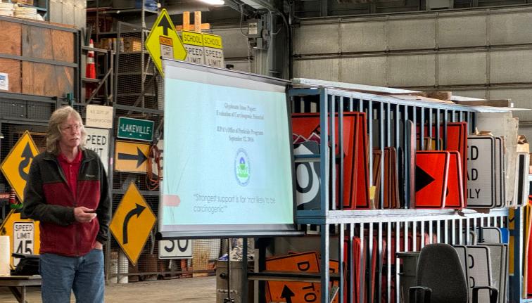 Person doing a presentation in a warehouse next to racks of traffic signs.