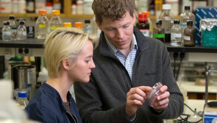 A faculty member and student examine a Petri dish in a lab.