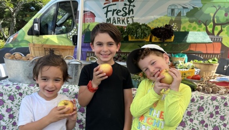 Three kids smile in front of a farm stand