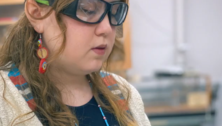 A student holds a clipboard while wearing safety goggles.
