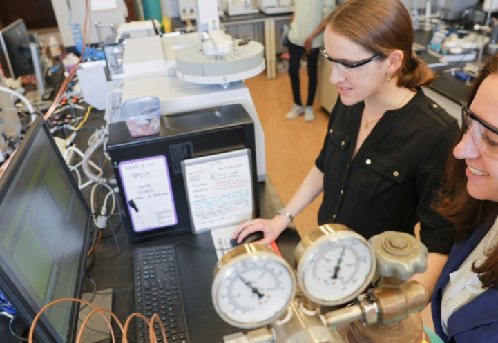 Two researchers wearing safety goggles look at something on a computer