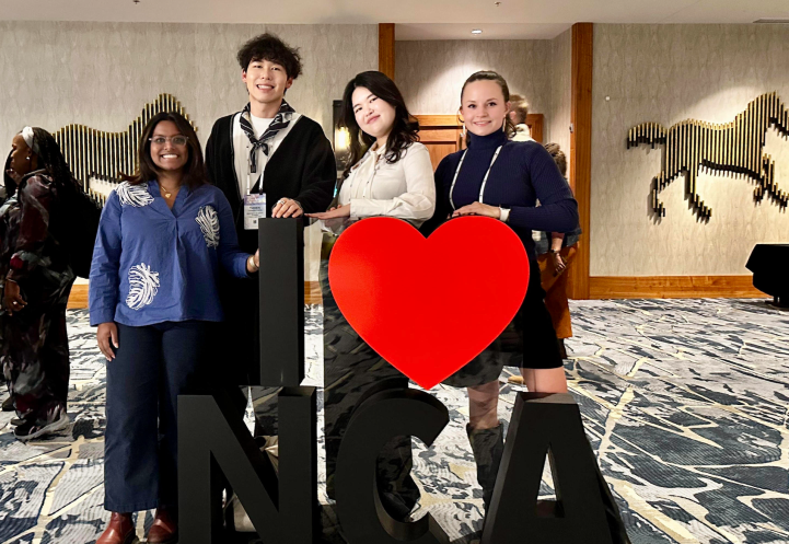 four people stand in front of a sign that reads I heart NCA