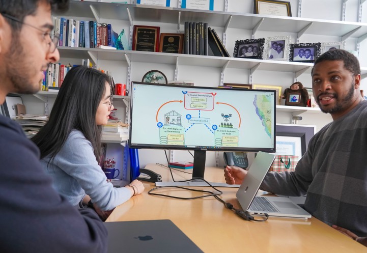 two men and a woman sit at a table talking with a schematic of farm and data on a view screen next to them