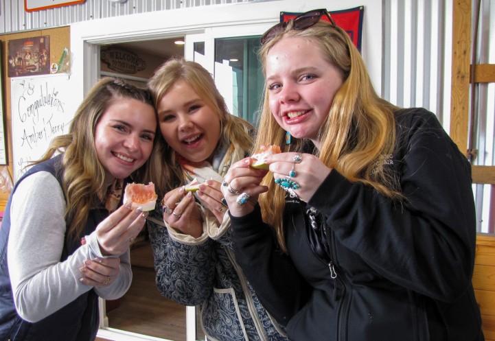 three woman stand together eating orange slices