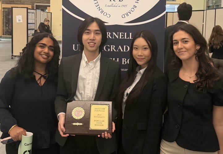 four students stand holding a plaque saying "peoples choice" in front of their poster