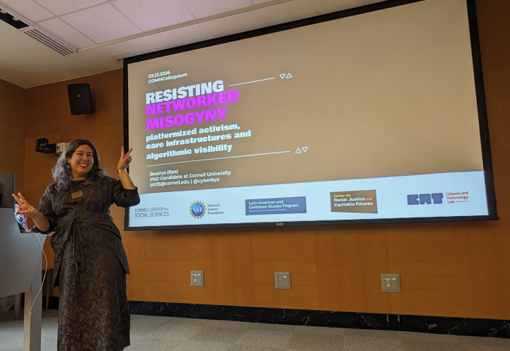 Beatrys Rodrigues presents on a stage in front of a screen