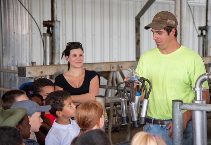 Cheryl on a farm tour with schoolkids. A farmer holds a miling machine in his hand, showing it to the kids.