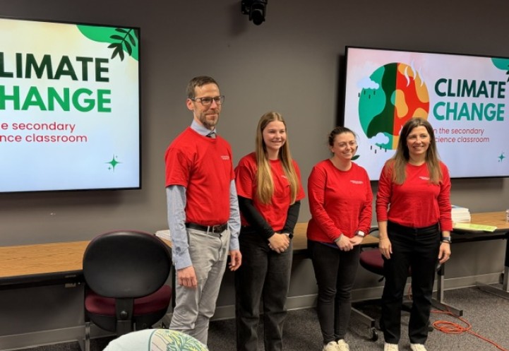 Four individuals in red t-shirts stand in a classroom next to screens displaying "CLIMATE CHANGE."