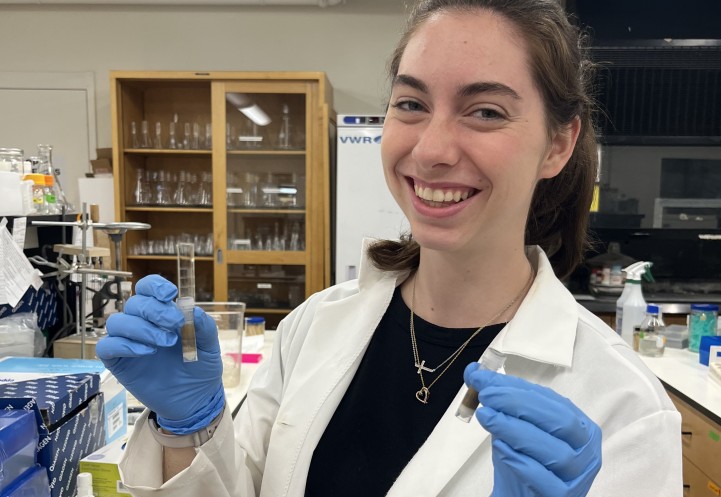 A woman holds two test tubes and smiles.